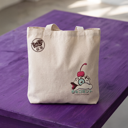 An off-white canvas tote bag with Japanese text and a Amiko Legends character graphic, resting on a purple wooden surface.