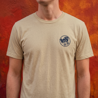 A man wearing a beige crewneck t-shirt with a Amiko Legends logo on navy blue  on the left chest, set against a textured orange and red background.