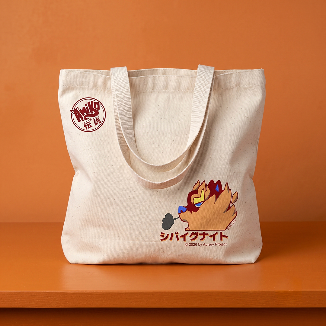 A cream-colored canvas tote bag with dual shoulder straps, featuring a circular red logo on the upper left and a Amiko Legends character with Japanese text on the front, set against a solid orange background.